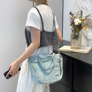 Detail of light blue nylon crossbody bag with drawstring handle on a wooden table