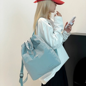 Frau trägt einen hellblaugrauen Nylon-Rucksack mit Kordelzug und verstellbaren Gurten