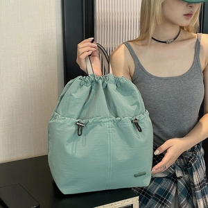 Detail of mint green drawstring backpack showing nylon texture and white stitching accents