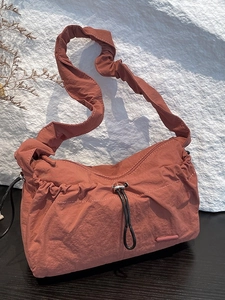 Fashionable clay red nylon cloud bag with pleated shoulder strap on stone background