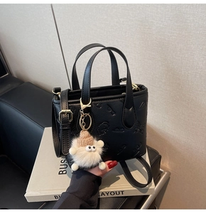 Detail view of black embossed crossbody bag with cartoon patterns and white pompom