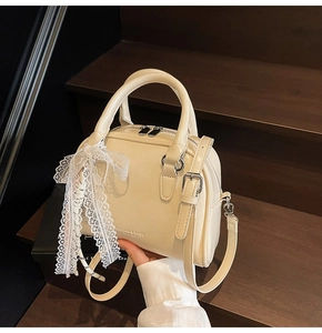 Detail of cream white leather Boston bag with lace bow on dark wooden stairs