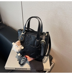 Detail of black embossed barrel bag with cartoon patterns and plush charm on a book