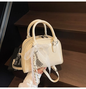 Detail of cream bowling bag with lace bow and silver tennis racket charm on wood steps