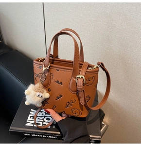 Detail of a brown printed crossbody bucket bag with cartoon patterns and plush charm