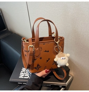 Detailed view of a brown leather bucket bag with cartoon prints and a plush doll charm