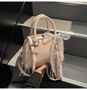 Close-up of light pink PU leather mini Boston bag featuring white lace bow and strap