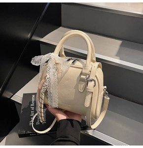 Detail of cream leather handbag with lace bow, woven charm and detachable shoulder strap