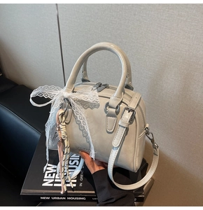 Detail of light grey bowling bag with lace bow charm on a decorative book backdrop