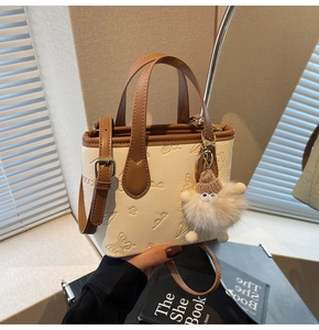 Detail of embossed cream crossbody bag with brown trim and plush charm accessory