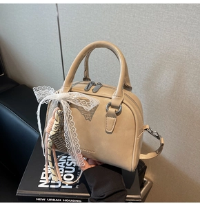 Detail of beige Boston bag with lace bow and woven pendant on a black book