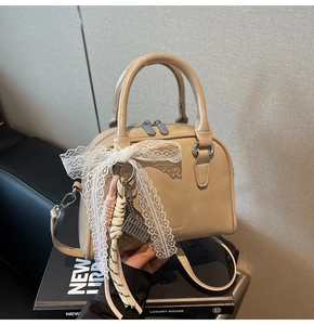 Detail of beige Boston bag featuring elegant lace bow and decorative tassel pendant charm
