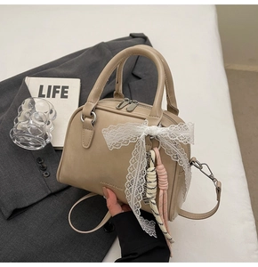 Detail of beige Boston bag with lace bow decoration and removable long shoulder strap