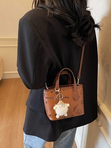 Brown mini tote bag with black graffiti prints and a white plush keychain accessory