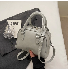 Close-up of light grey bowling handbag with embossed logo and textured leather finish