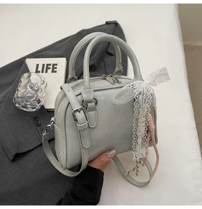 Detail of light gray leather bowling bag with lace bow and stylish hanging strap