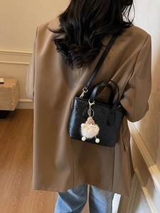 Chic black embossed crossbody bucket bag with plush charm on a model in a warm interior