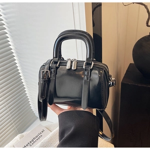 Close-up of black glossy mini Boston bag with silver hardware and adjustable strap
