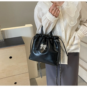 Detail of black drawstring bucket bag with shiny silver bow and metal chain strap