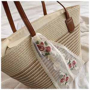 Detail of straw tote bag featuring delicate white lace ribbons and pink floral embroidery