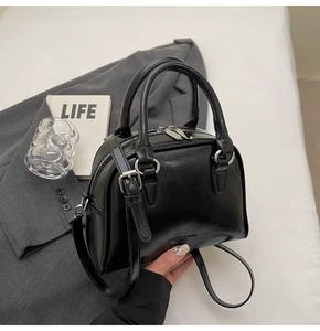 Detail of a shiny black bowling handbag with silver hardware on a grey blazer