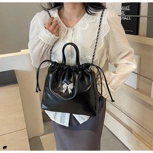 Detail of black drawstring bucket bag with silver bow charm and elegant chain strap