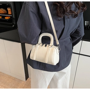 Detail view of cream Boston bag in patent leather worn with detachable shoulder strap