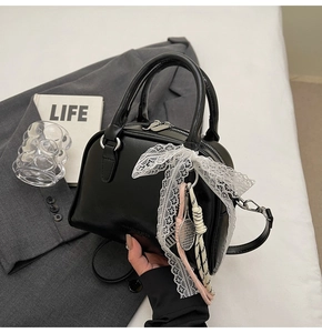 Detail view of a black bowling bag with lace bow and tennis racket charms on a white table