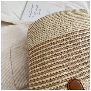 Close-up of woven straw bag showing striped texture and brown lychee leather strap