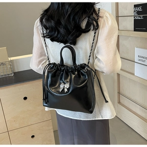 Detail of glossy black leather bucket bag featuring a silver metal bow and drawstring