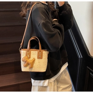 Détail d'un sac seau crème et marron avec motifs gaufrés et breloque chien sur modèle