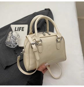 Detail of cream bowling bag with lychee texture and silver hardware on white table