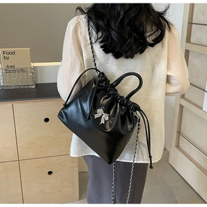Detail of black drawstring bucket bag featuring a rhinestone bow and metal chain strap