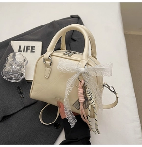 Detail of cream-colored bowling bag with delicate lace bow and decorative charms