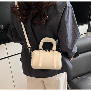 Model wearing a cream white Boston handbag with a minimalist grey shirt in modern room