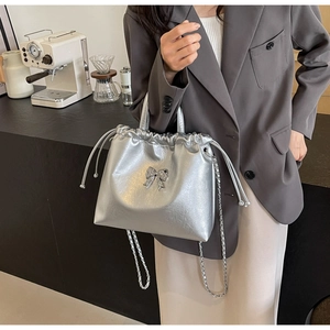 Silver metallic tote with bow detail and chain strap shown in a modern interior setting