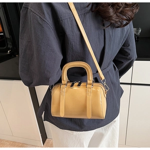 Detailed view of ginger yellow mini Boston bag with shiny finish and shoulder strap
