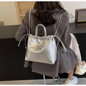 Close-up of a silver pleated bucket bag with a 3D bow detail and metal chain strap