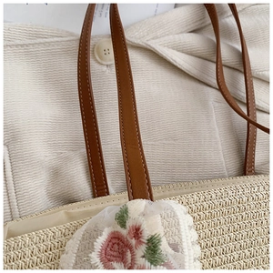 Close-up of straw woven tote bag featuring floral lace embroidery and brown leather straps