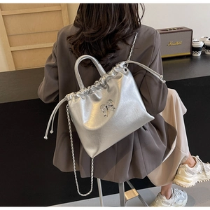 Silver metallic bow tote bag with drawstring closure and chain strap on a model