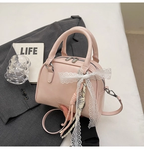 Detail of pink Boston bag featuring a white lace bow and woven rope pendant charm