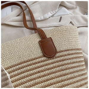 Detailed view of woven straw tote bag texture and brown leather shoulder strap joint