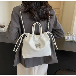 Detail of white drawstring bucket bag with silver metal bow and chain shoulder strap