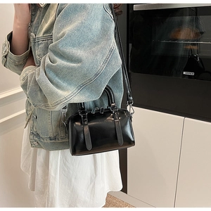Mini black Boston handbag with shiny leather and shoulder strap shown on a model