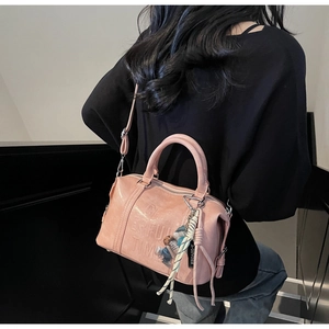 Detailed view of pink Boston bag with embossed text and doll pendant shown on model