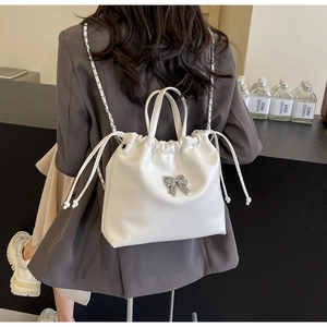 Detail of white pleated backpack with silver metal bow and leather chain strap