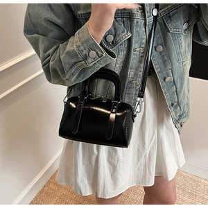 Glossy black mini Boston bag styled with a denim jacket and white skirt on a model