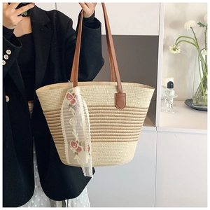 Detailed view of woven straw tote bag featuring striped pattern and floral lace ribbon