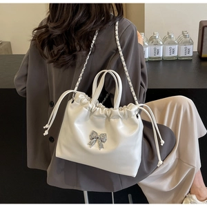 Detail of white drawstring bag with silver bow hardware and elegant chain strap