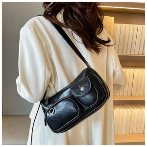 Detail of a black multi-pocket crossbody bag with silver rings on a white blazer
